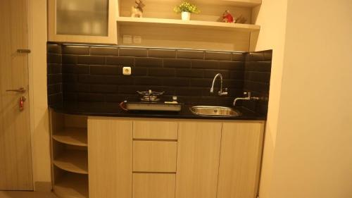 een keuken met een wastafel en een zwart betegelde muur bij Apartemen Grand Kamala Lagoon by Cheapinn in Bekasi