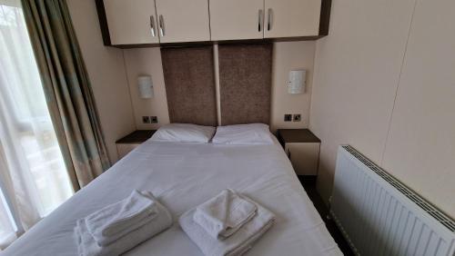 um pequeno quarto com uma cama branca e toalhas em Winchelsea Sands Holiday Park em Winchelsea