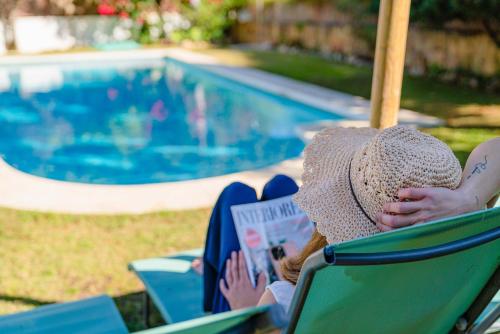 Eine Frau, die auf einem Stuhl sitzt und ein Buch am Pool liest. in der Unterkunft Villa 10 Luxe by Lirios Village Marbella in Marbella