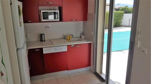 une cuisine avec des placards rouges et un four micro-ondes ainsi qu'une piscine dans l'établissement Villa 8 personnes - piscine privative - Golf- Plage, à Saint-Cyprien