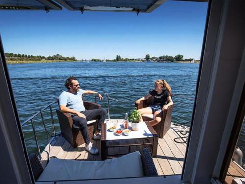 金洛伊的住宿－Attractive houseboat in Kinrooi with terrace，两个人坐在水面上的船上