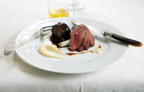 a plate of food with meat and a knife and fork at Monachyle Mhor Hotel in Lochearnhead
