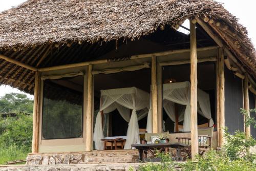 una casa con techo de paja, mesas y sillas en Soroi Cheetah Tented Camp en Mwatate