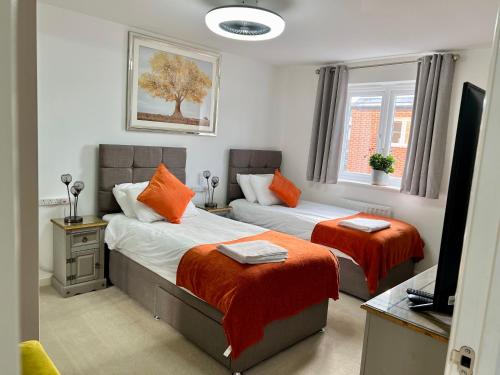 1 Schlafzimmer mit 2 Betten mit orangefarbener Bettwäsche und einem TV in der Unterkunft Driver Way in Wellingborough