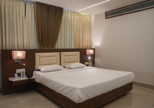 a bedroom with a large white bed with two lamps at Hotel JK Celebration in Jabalpur