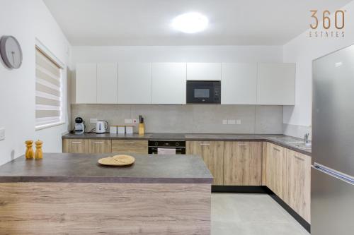 La cuisine est équipée de placards blancs et d'un réfrigérateur en acier inoxydable. dans l'établissement Lovely 3BR Apt with Private Balcony & Views in Mgarr by 360 Estates, à Mġarr