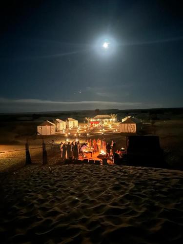 a group of people standing on a beach at night at Ibra desert Camp in Merzouga