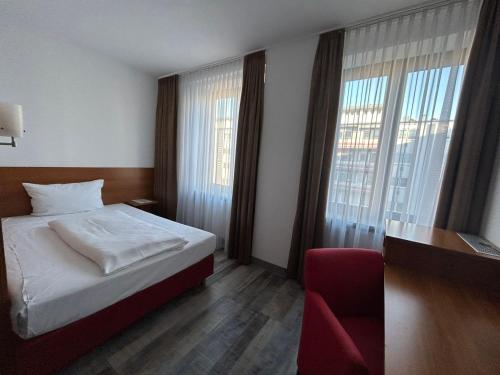 a bedroom with a bed and a chair and windows at Hotel Fackelmann in Nürnberg