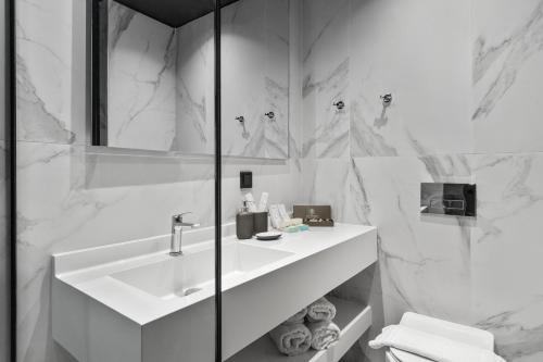 La salle de bains blanche est pourvue d'un lavabo et d'un miroir. dans l'établissement Azur Hotel Volos, à Vólos