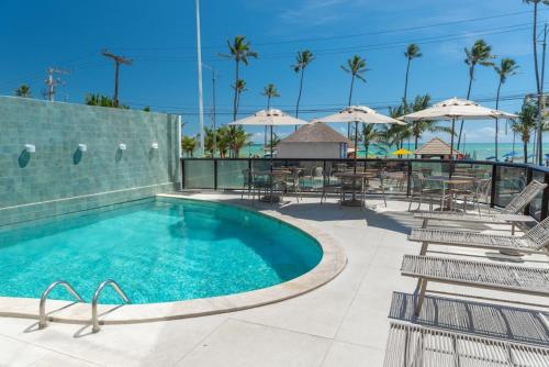 una piscina con sillas, mesas y sombrillas en Hotel Brisa Tower Maceió en Maceió