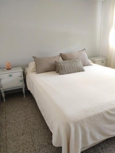 1 cama blanca grande con almohadas y mesita de noche en Alquiler Casa con pileta en Godoy Cruz