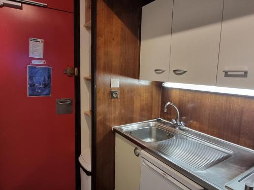 Il comprend une petite cuisine avec un évier et une porte rouge. dans l'établissement Studio fonctionnel avec accès direct aux pistes - FR-1-181-2605, à Aime La Plagne
