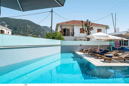 a pool with chairs and an umbrella and a house at BLUE STAR APARTHOTEL in Nydri