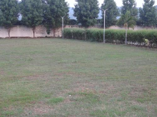 a large grass field with trees and a fence at The Royal Residency in Rājgīr