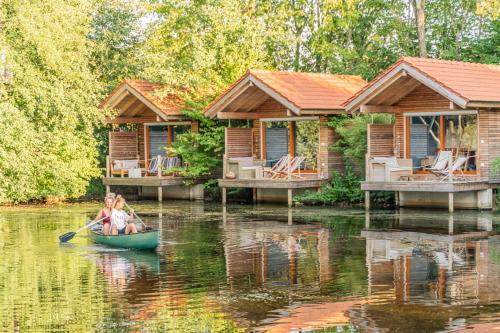 Eine Frau, die vor zwei Cottages auf einem Fluss ein Kanu paddelt in der Unterkunft Baumhaushotel Oberbayern in Jetzendorf