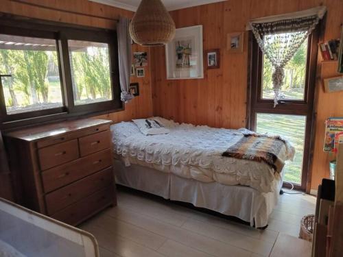 a bedroom with a bed and a dresser and windows at Hermosa cabaña con hot tub. in Talagante