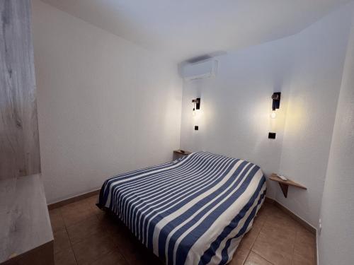 ein Schlafzimmer mit einem gestreiften Bett in einem weißen Zimmer in der Unterkunft Appartement au Hameau des Issambres Le Pamakior in Les Issambres