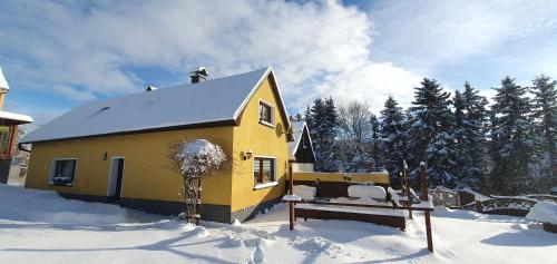 ein gelbes Haus im Schnee mit einer Bank in der Unterkunft Ferienhaus Reichel in Kurort Oberwiesenthal