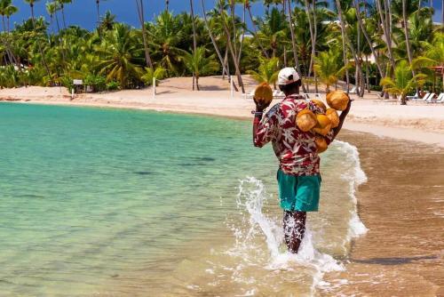 a man walking in the water with coconuts on his back at Exclusive Villa * private Beach and Housekeeping in Punta Cana
