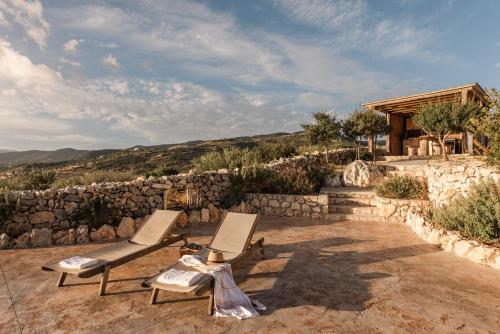 2 Stühle auf einer Terrasse mit einer Steinmauer in der Unterkunft Anemomilos in Koríthion