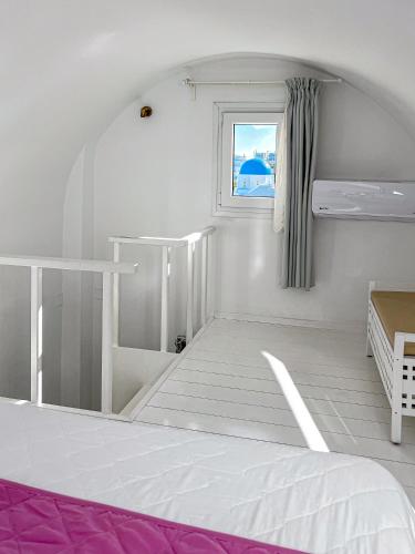 a white room with a bed and a window at Reverie Santorini Hotel in Firostefani