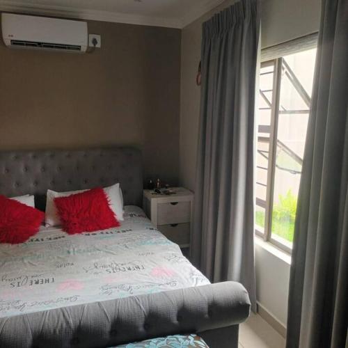 Un dormitorio con una cama con almohadas rojas y una ventana en elawini estate, en Boschrand