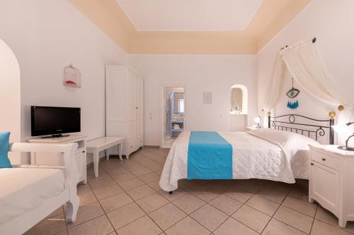 a white bedroom with a bed and a tv at Reverie Santorini Hotel in Firostefani