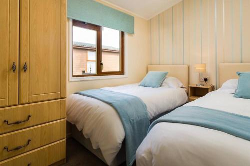 Luxury 3 bedroom lodge with free in lodge wifi في كارنفورث: غرفة نوم بسريرين ونافذة