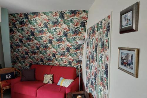 - un canapé rouge dans une chambre avec papier peint à fleurs dans l'établissement Apartment with balcony close to the beach, à Cabourg