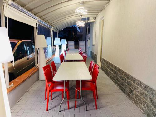 una fila de mesas con sillas rojas y un coche en hotel roby, en Rímini