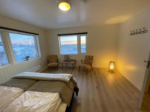 a bedroom with a bed and two chairs and windows at Å, the far end of Lofoten, top apartment. in Sørvågen