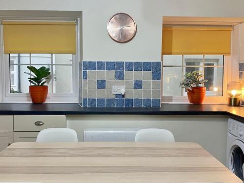een keuken met een tafel en twee ramen met planten bij Beautifully decorated bright and cosy cottage in Aveton Gifford