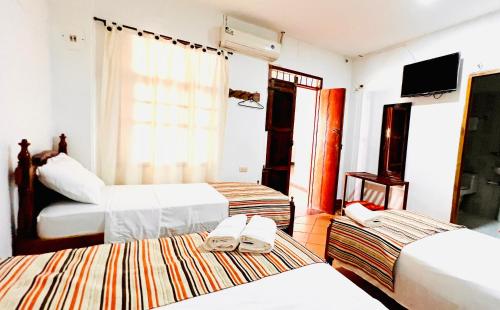 a hotel room with three beds and a television at Hotel Villa de Mompox in Mompos