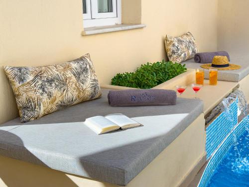 a bed with a book and glasses of wine at Reverie Santorini Hotel in Firostefani