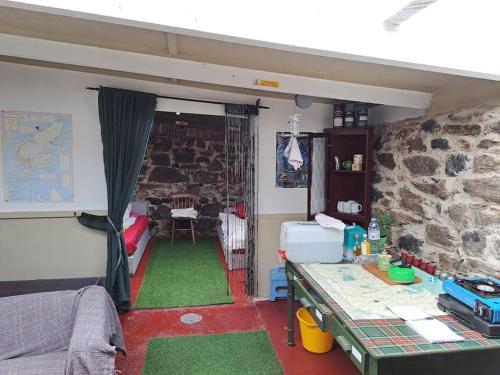 a room with a stone wall and a room with green carpet at Squealing Pig Bothy in Bragor