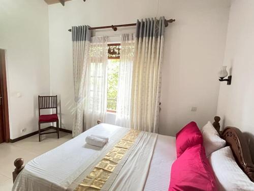 a bedroom with a bed with pink pillows and a window at Caro Villa in Induruwa