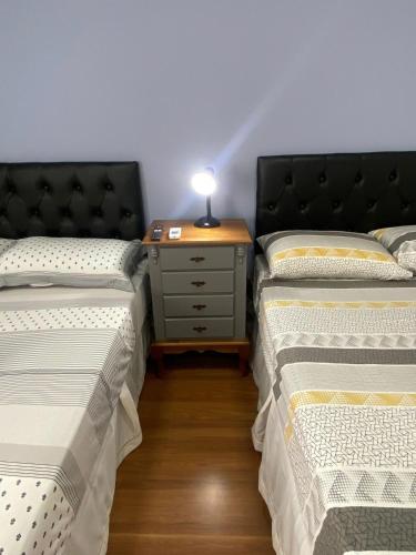 Cette chambre comprend deux lits et une table avec une lampe. dans l'établissement EDIFÍCIO KARINE - Studio 103 Deluxe, à Joinville