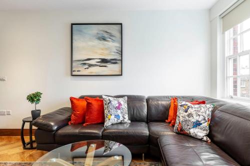 sala de estar con sofá de cuero marrón con almohadas en Colourful South Kensington Home, en Londres