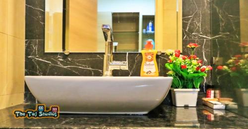 a bathroom sink with a faucet and flowers on a counter at Ghumloo/com - Super Deluxe Stay at Finest Mall Gaur City (Bar, Club, Rajhansh Cinemas, Food Court, SuperMart etc..) in Ghaziabad