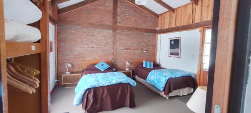 1 dormitorio con 2 camas en una habitación con una pared de ladrillo en Chacra Kaiken Lodge en Perito Moreno