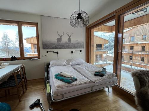 a bedroom with a bed and a table and windows at AlmApp Nassfeld in Sonnenalpe Nassfeld