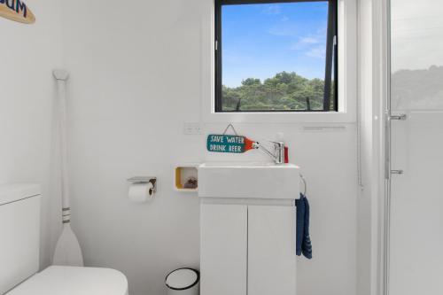 La salle de bains blanche est pourvue d'un lavabo et d'une fenêtre. dans l'établissement Pacific Bay HQ - Tutukākā Holiday Unit, à Tutukaka