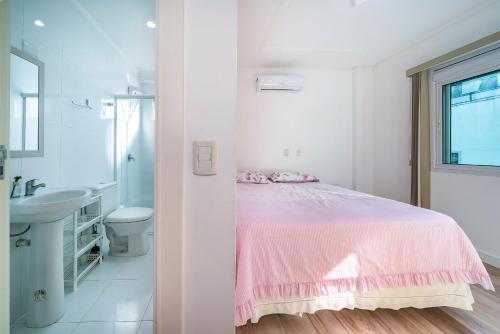 Dormitorio blanco con cama rosa y lavabo en Aluguel Apartamento 3 quartos sendo 1 suíte em Bombinhas, en Bombinhas