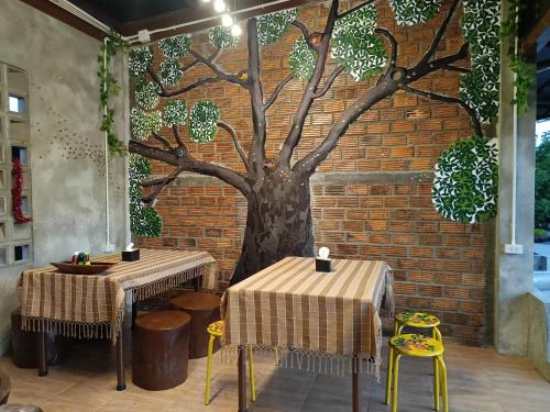 dos mesas y un mural de árbol en una pared de ladrillo en ต้นโพธิ์โฮมสเตย์ 