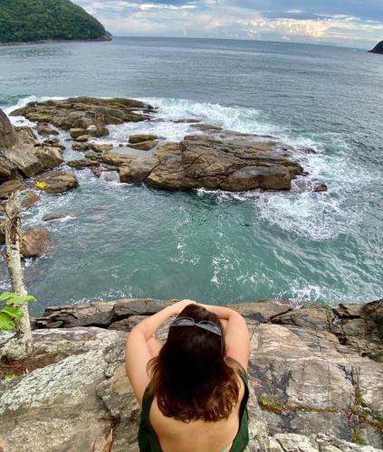 a woman sitting on a cliff looking at the ocean at Casa com vista a praia da Barra do Sahy in Barra do Sahy