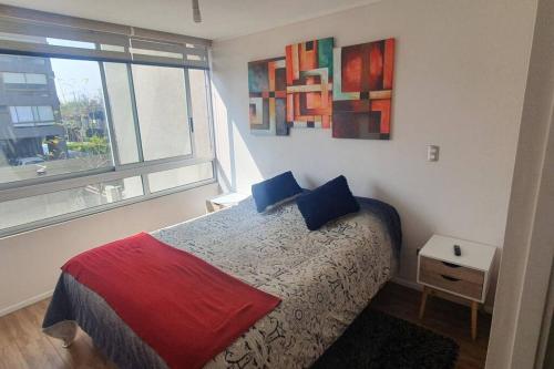 Un dormitorio con una cama con almohadas azules y una ventana en Espectacular departamento Ñuñoa, en Santiago