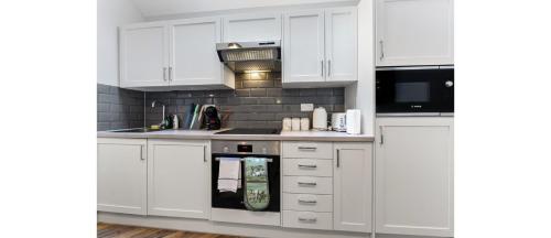 a white kitchen with white cabinets and a microwave at Cozy 1 BD Flat in London! in Romford