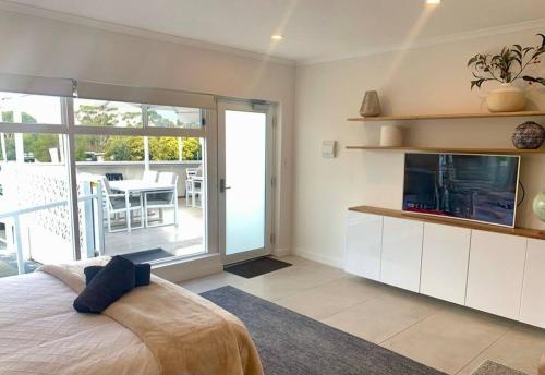 1 dormitorio con cama, TV y balcón en Adorable Studio next to cafe, walk to beach!, en Orford