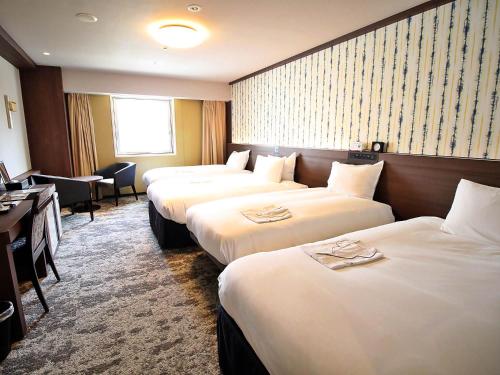 高知市にあるリッチモンドホテル高知のベッド3台とデスクが備わるホテルルームです。