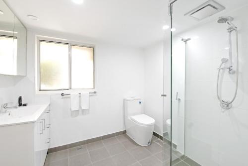 a white bathroom with a toilet and a glass shower at A Quaint Darlinghurst Cottage in Sydney